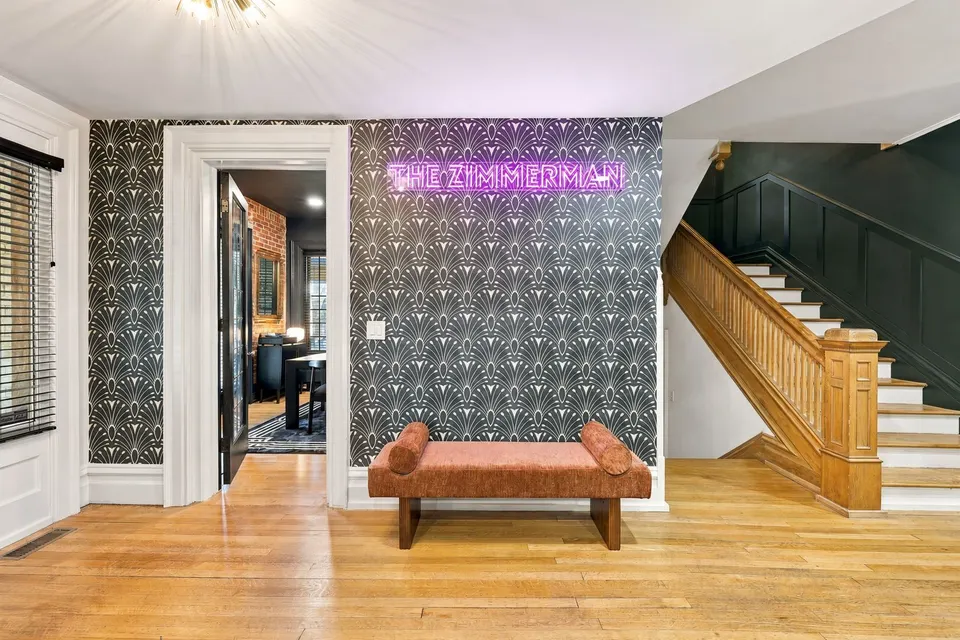 The front hall: neon sign, fan wallpaper, a velvet bench and the oak staircase