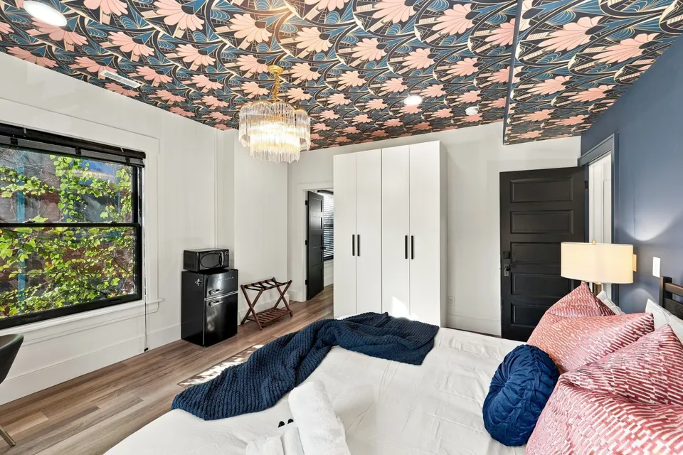 A guest room under a floral wallpapered ceiling and crystal chandelier
